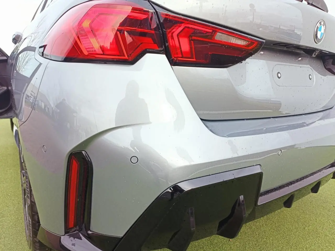 Vue 3/4 arrière droite d'une BMW Série 1 gris Skyscraper avec feux LED distinctifs et diffuseur noir brillant.