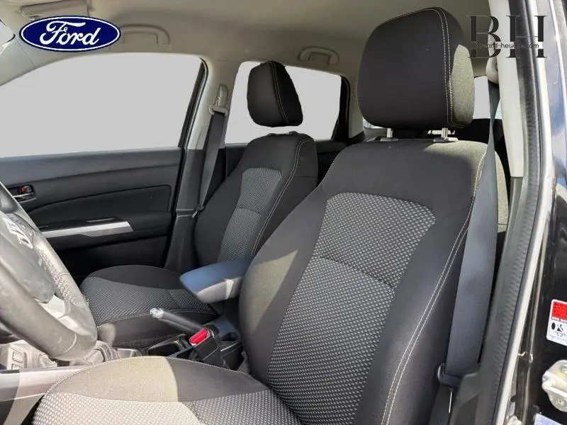 Vue intérieure côté conducteur du Suzuki Vitara Cosmic Black Pearl, sièges tissu noir avec accoudoir central et volant cuir.