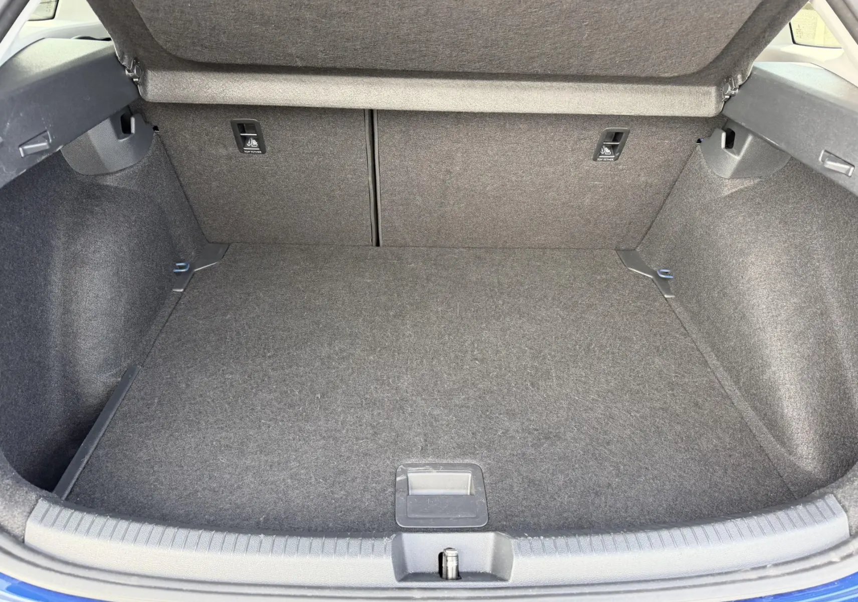 Coffre ouvert vu de l'arrière d'un Volkswagen Taigo bleu, montrant un espace de chargement propre et tapissé de tissu gris.