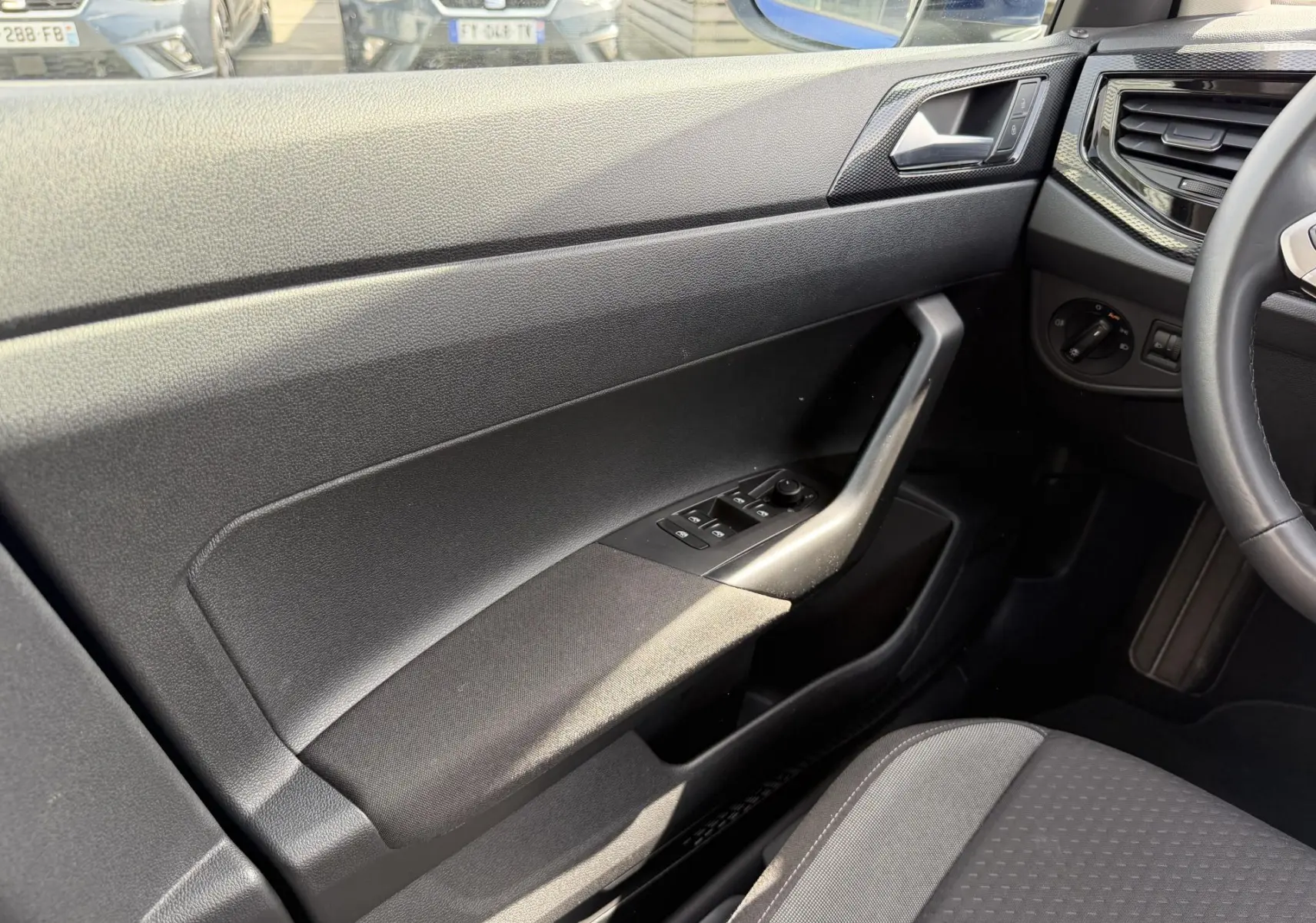 Intérieur côté conducteur du Volkswagen Taigo 2025, montrant la portière noire avec commandes des vitres et partie du volant cuir multifonctions.