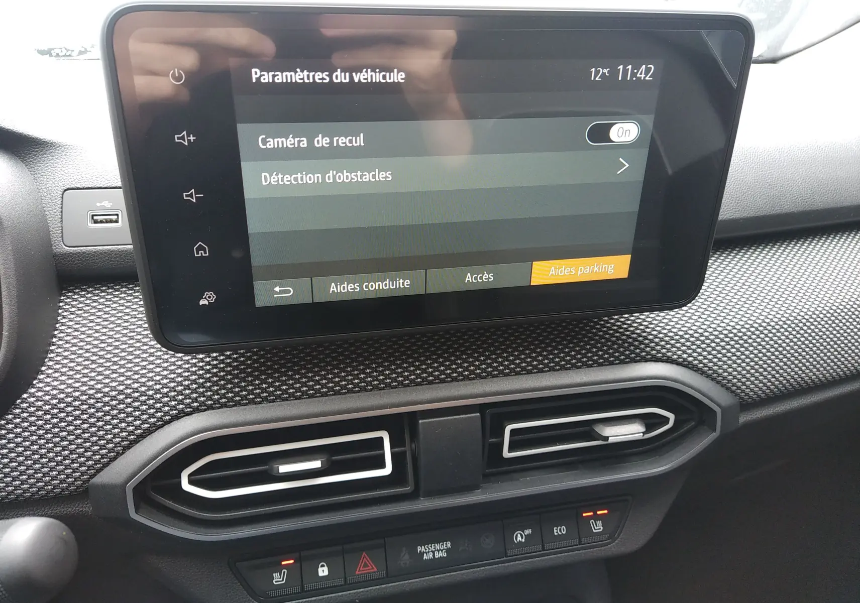 Écran tactile central affichant les paramètres d'aide au stationnement dans l'habitacle du Dacia Sandero bleu Iron 2025.