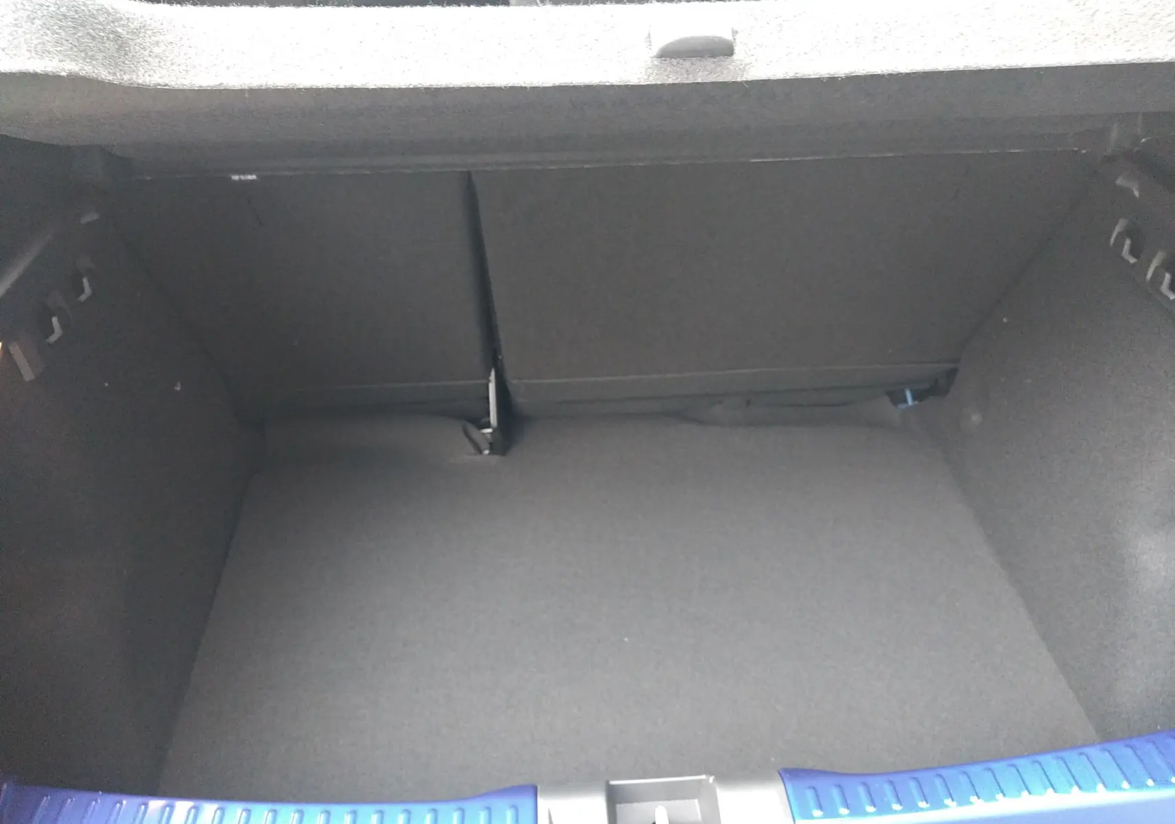 Coffre ouvert vu de face d'une Dacia Sandero 2025 bleu iron, montrant l'espace de rangement vide et la garniture intérieure noire.