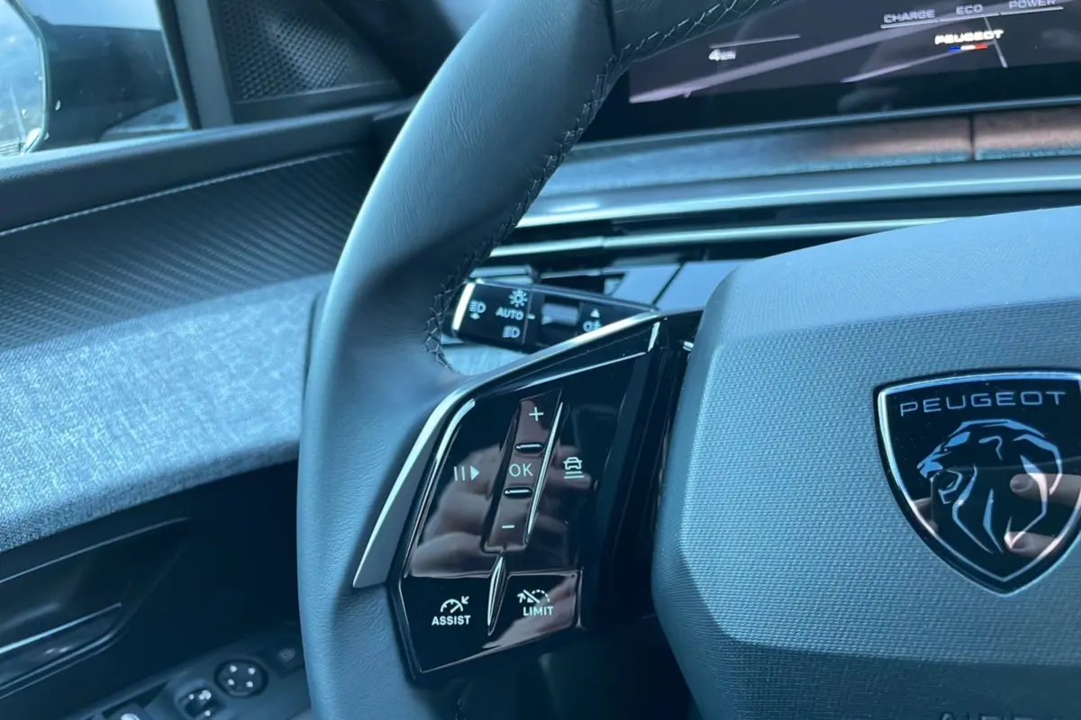 Gros plan sur le volant cuir du Peugeot 5008 Hybrid 145 Allure Plus gris titane avec commandes multifonctions et logo lion.