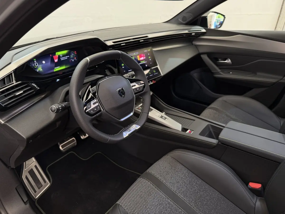 Intérieur avant droit de la Peugeot 308 Hybrid 136 e-DCS6 GT 2024 avec volant cuir et écran tactile couleur.
