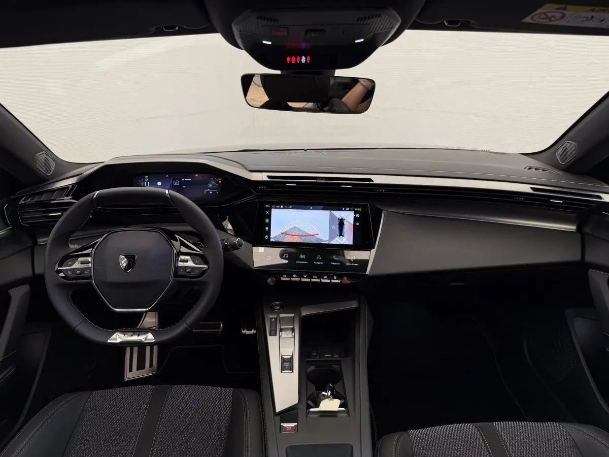 Intérieur noir de la Peugeot 308 Hybrid 136 e-DCS6 GT 2024, vue frontale du tableau de bord et volant multifonctions.