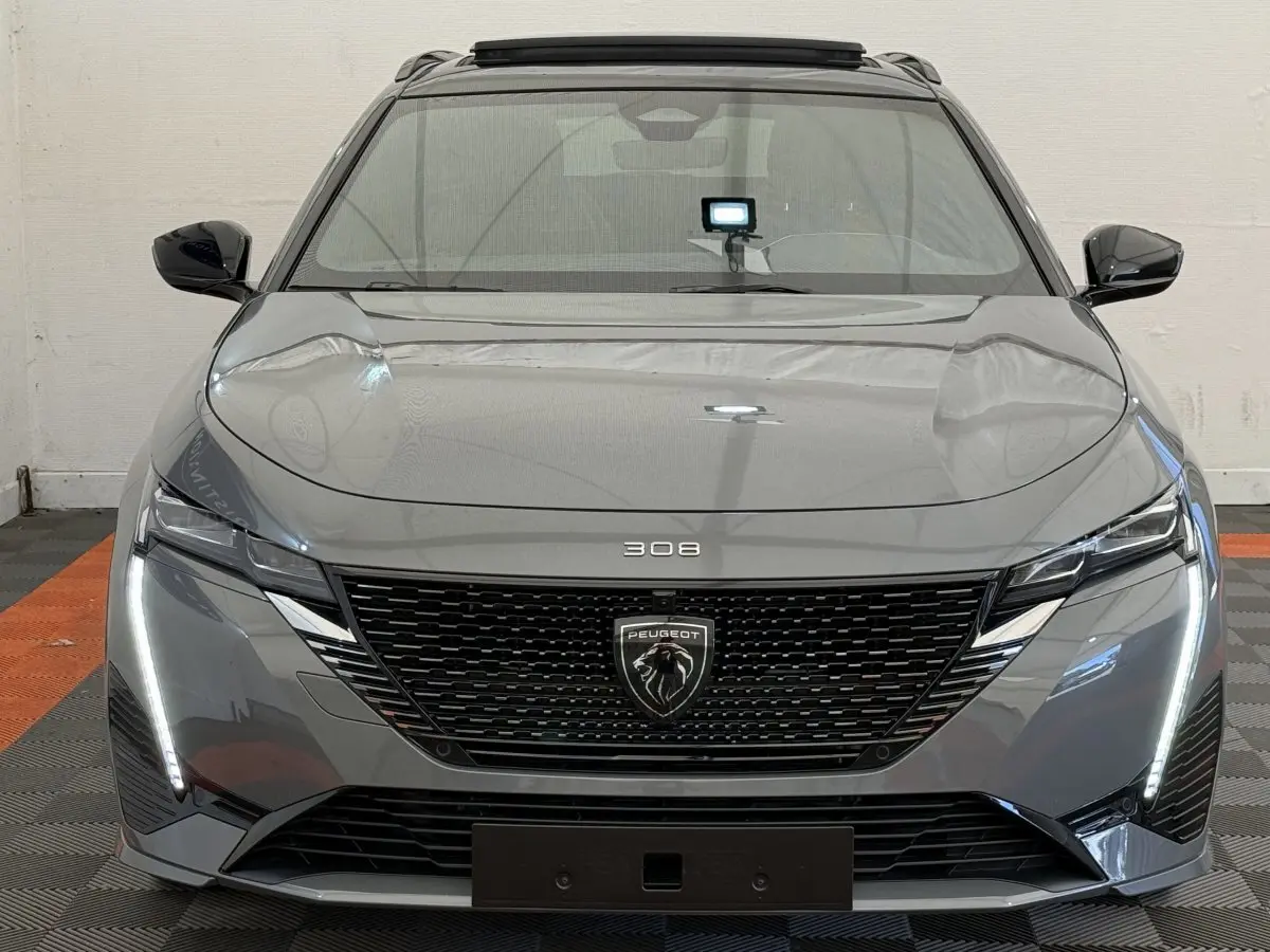 Vue frontale d'une Peugeot 308 Hybrid 136 e-DCS6 GT gris foncé avec calandre noire et feux LED verticaux allumés.