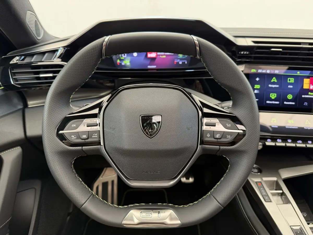 Volant cuir noir avec logo Peugeot et badge GT, vue frontale du poste de conduite de la 308 Hybrid 2024.