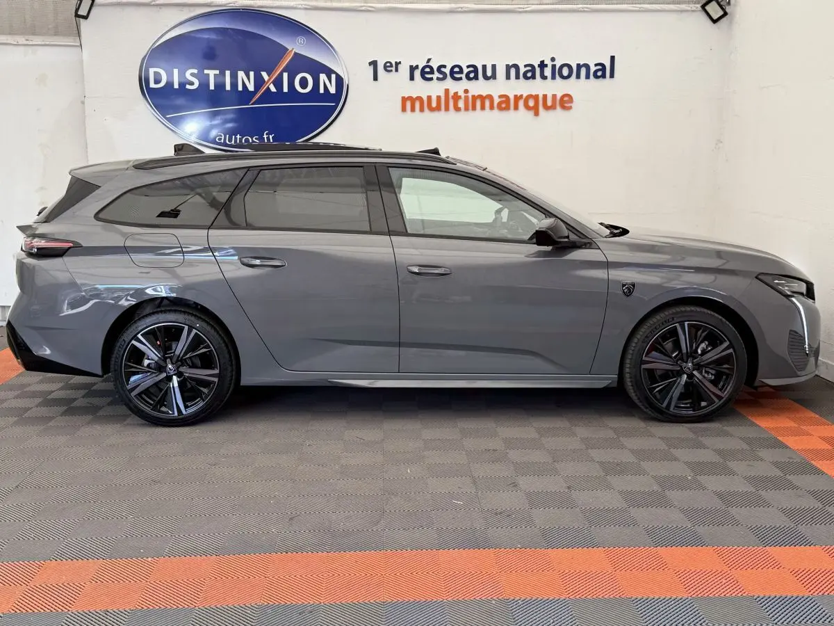 Profil droit d'une Peugeot 308 Hybrid 136 e-DCS6 GT gris foncé avec jantes noires et toit panoramique visible.