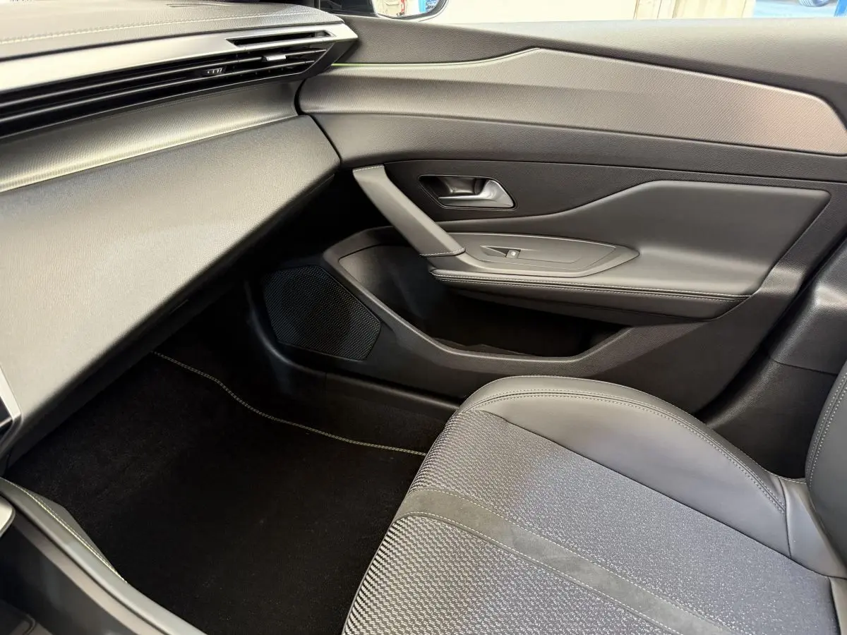 Intérieur côté passager de la Peugeot 308 Hybrid 136 e-DCS6 GT 2024 en gris foncé, avec siège et porte élégants.