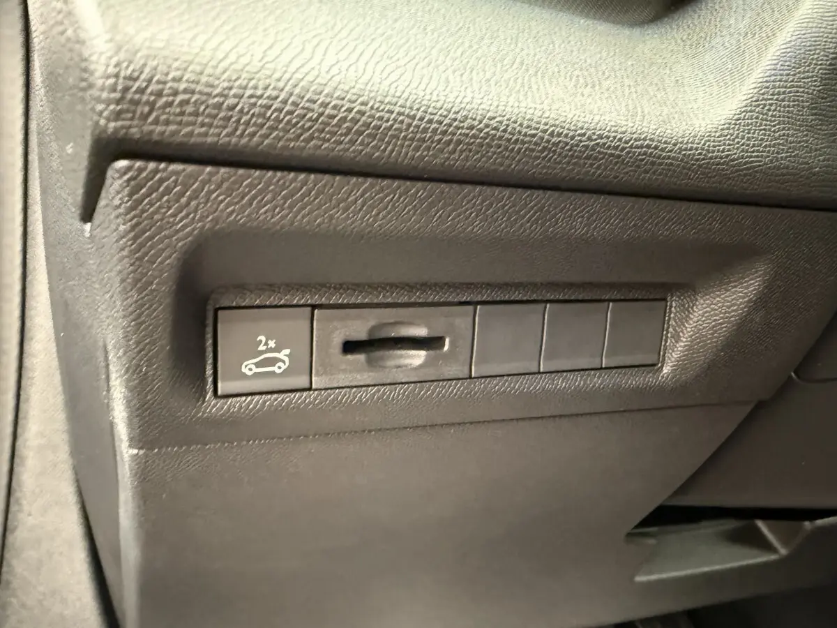 Gros plan sur le bouton d'ouverture du coffre côté gauche dans l'habitacle gris foncé du Peugeot 308 Hybrid 2024.