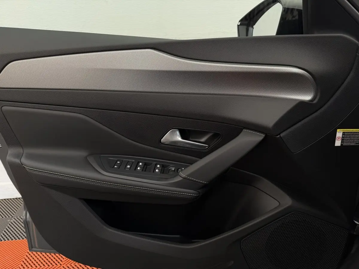 Gros plan sur la porte côté conducteur de la Peugeot 308 Hybrid gris foncé, avec commandes électriques et finition cuir noire.