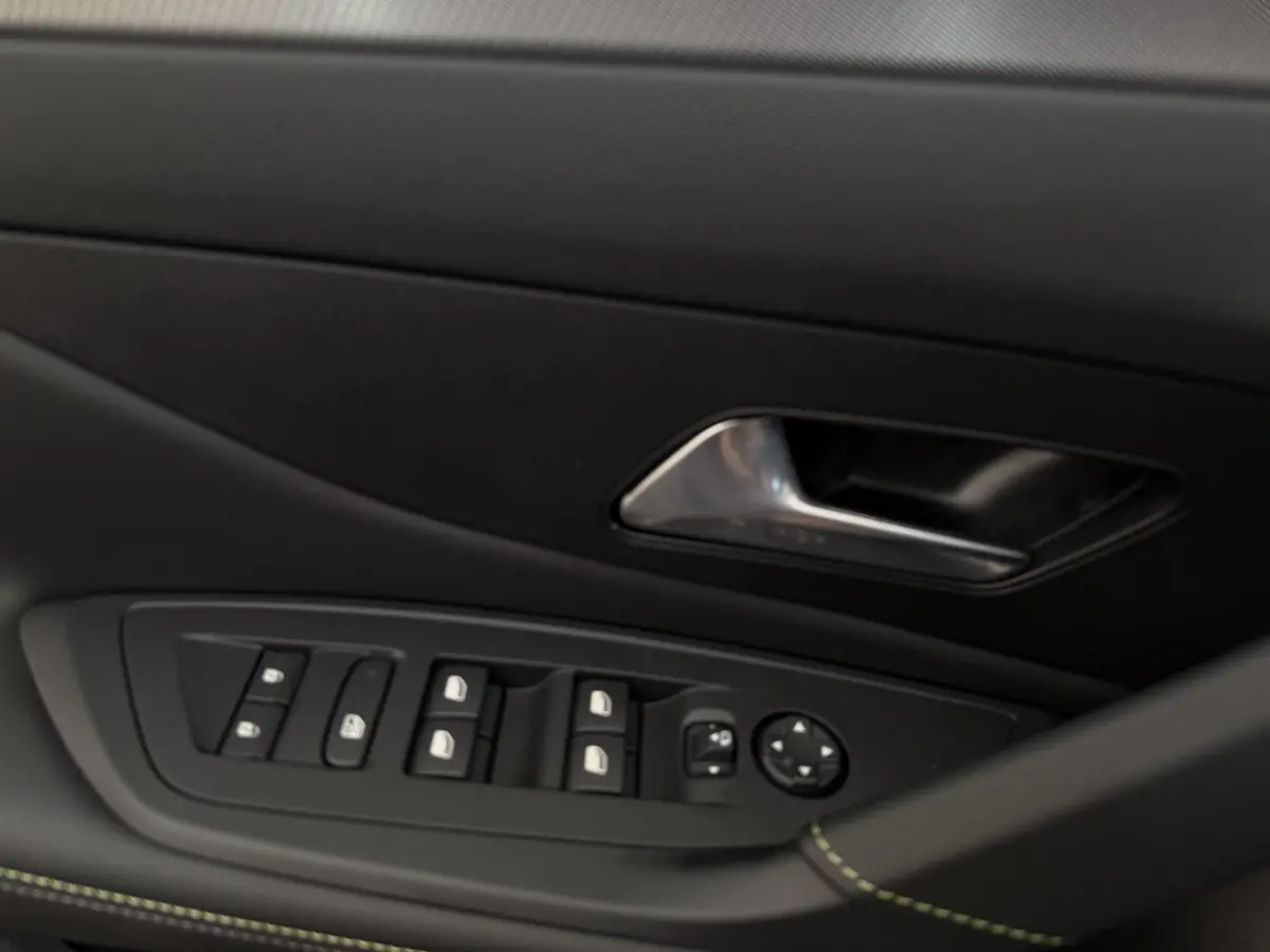 Gros plan sur la porte côté conducteur de la Peugeot 308 Hybrid gris foncé, avec commandes des vitres et poignée métal.