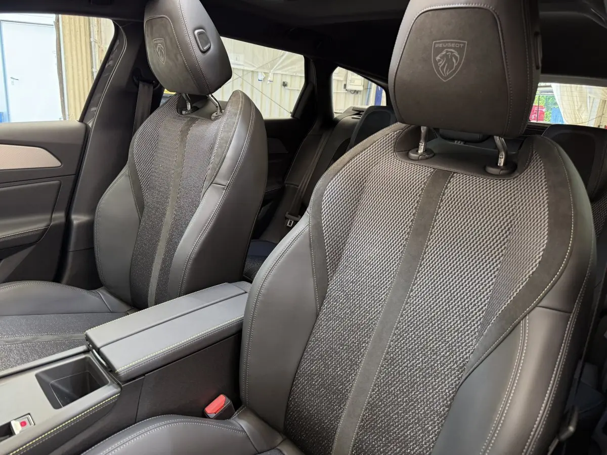 Gros plan sur les sièges avant gris foncé en cuir et tissu du Peugeot 308 Hybrid 2024 avec logo Peugeot brodé sur les appuie-têtes.