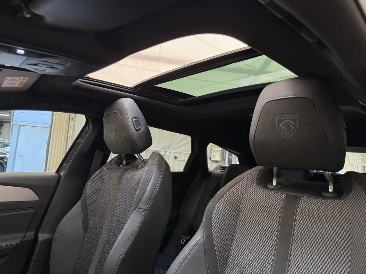 Vue intérieure rapprochée des sièges avant gris foncé avec logo Peugeot sur les appuie-têtes et toit ouvrant panoramique.