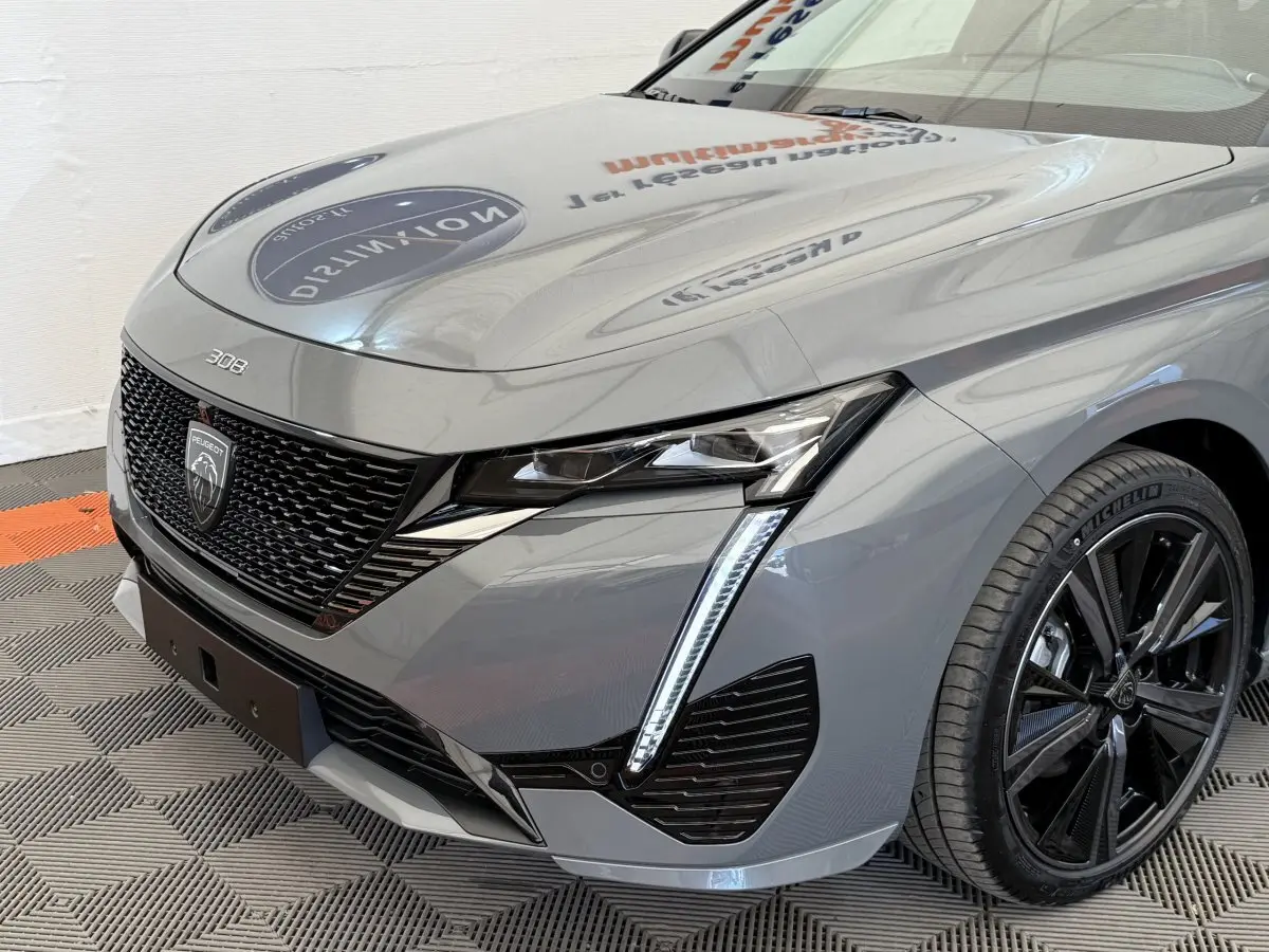 Vue 3/4 avant droit d'une Peugeot 308 Hybrid 136 e-DCS6 GT gris foncé avec phares LED et jantes noires.