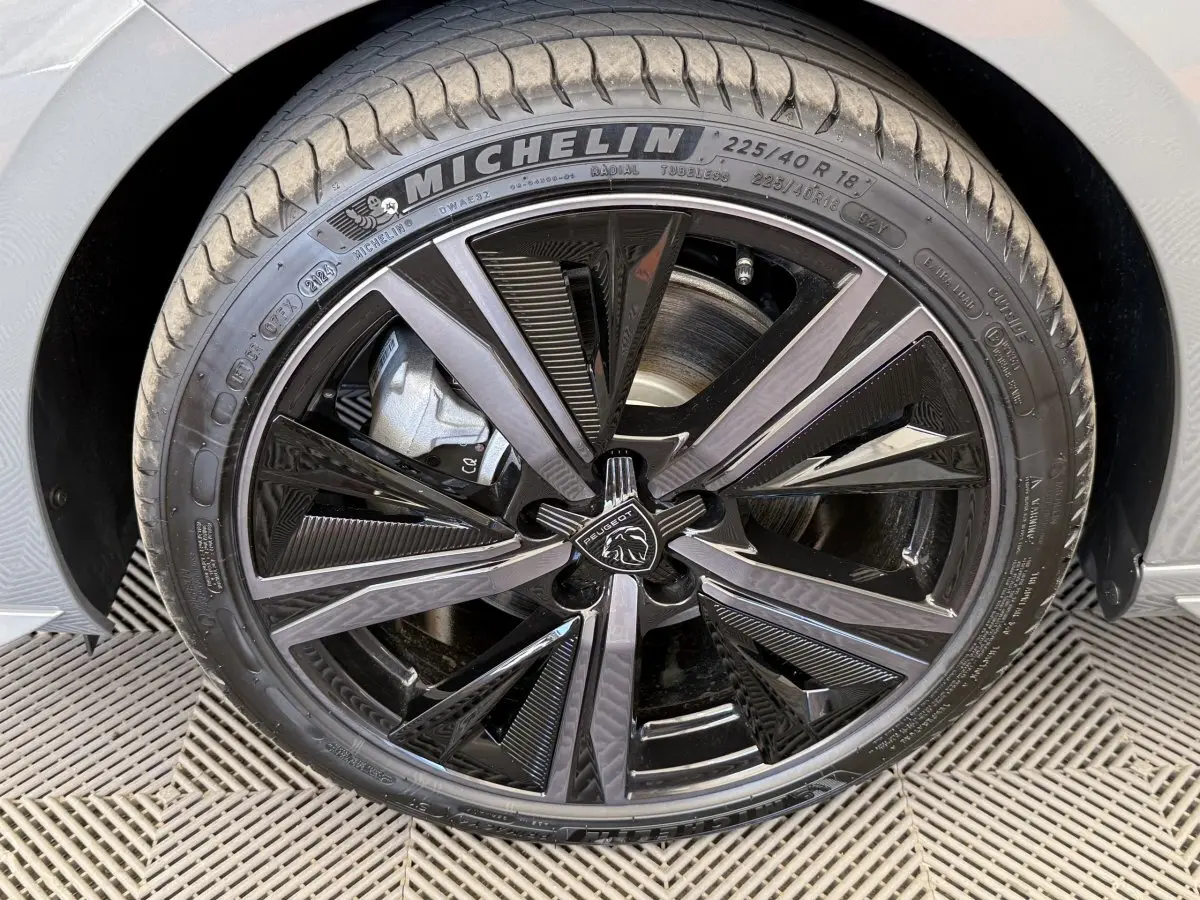 Gros plan sur la roue avant droite gris foncé de la Peugeot 308 Hybrid 136 e-DCS6 GT avec jante noire brillante et logo Peugeot.
