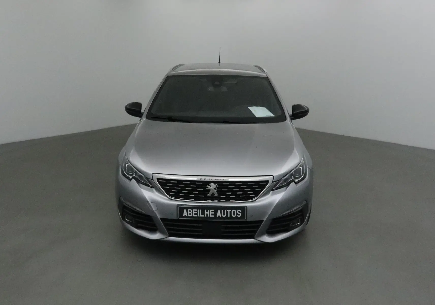 Peugeot 308 SW gris Artense vue de face dans un studio, calandre et logo lion bien visibles.