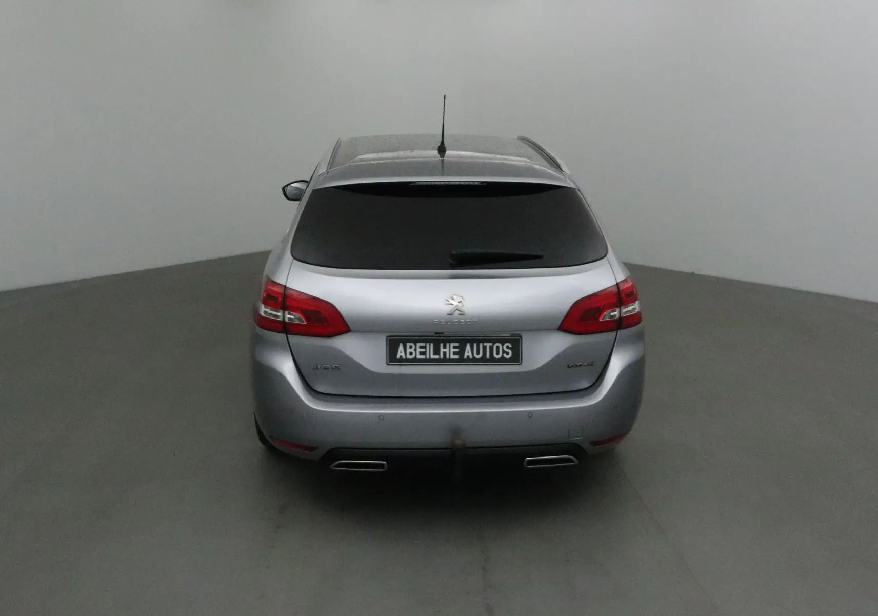 Vue arrière d'une Peugeot 308 SW gris Artense avec vitres teintées et double sortie d'échappement visible.