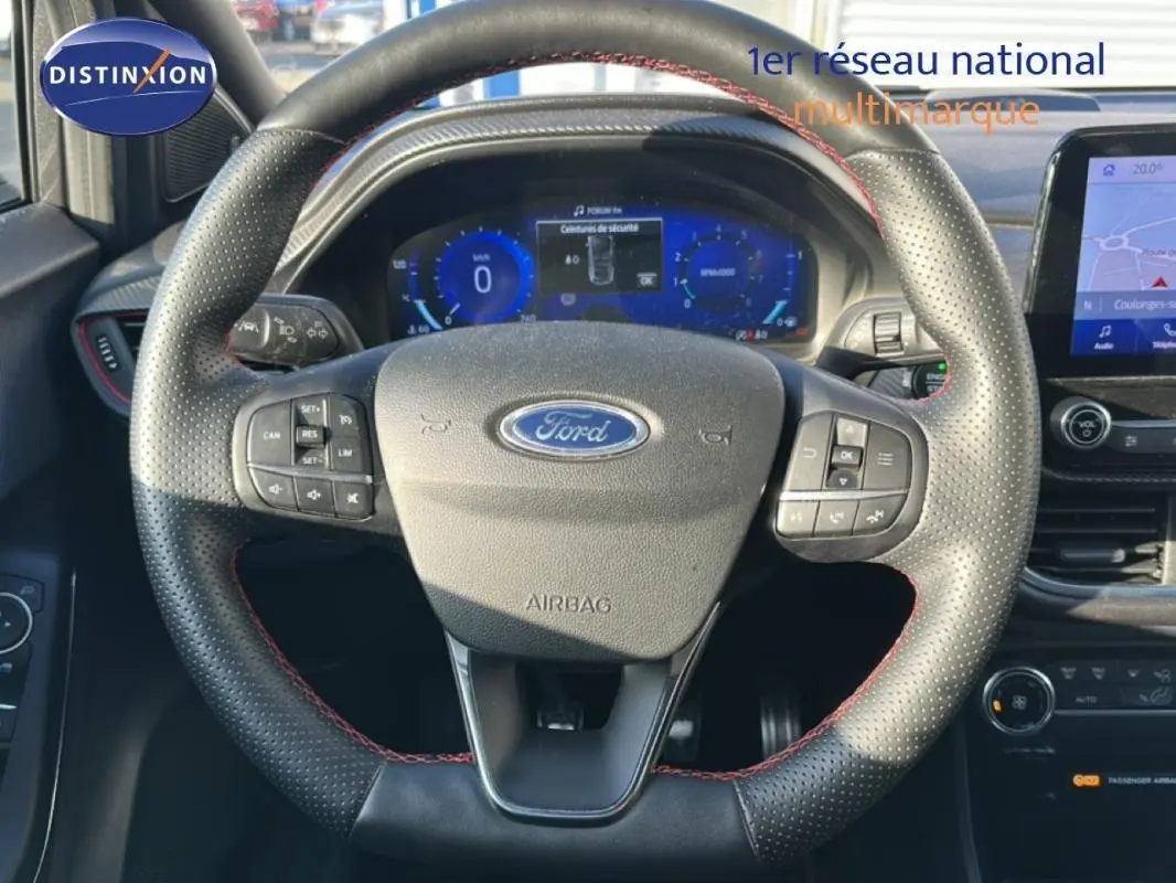 Vue centrée sur le volant perforé noir avec surpiqûres rouges du Ford Puma 2020, tableau de bord digital et écran tactile visibles.