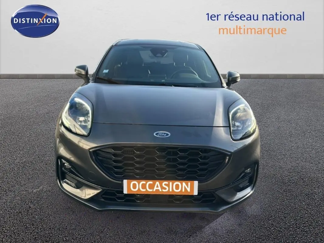 Vue frontale d'une Ford Puma gris foncé avec calandre noire et feux avant allumés sur fond neutre.