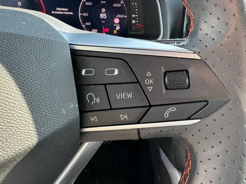 Gros plan sur les commandes au volant côté gauche du SEAT Arona 2025, volant cuir perforé avec surpiqûres rouges.