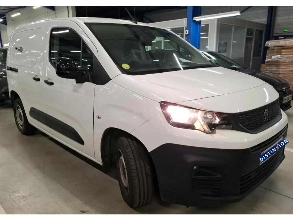 Vue 3/4 avant droit d'un Peugeot Partner Fourgon blanc 2022 avec phares allumés et protections noires sur les bas de caisse.