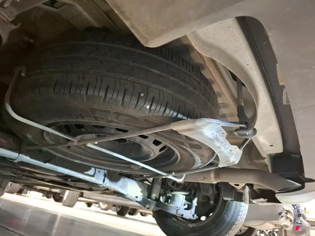 Vue en contre-plongée sous le Peugeot Partner Fourgon blanc, montrant la roue de secours fixée sous le châssis arrière.