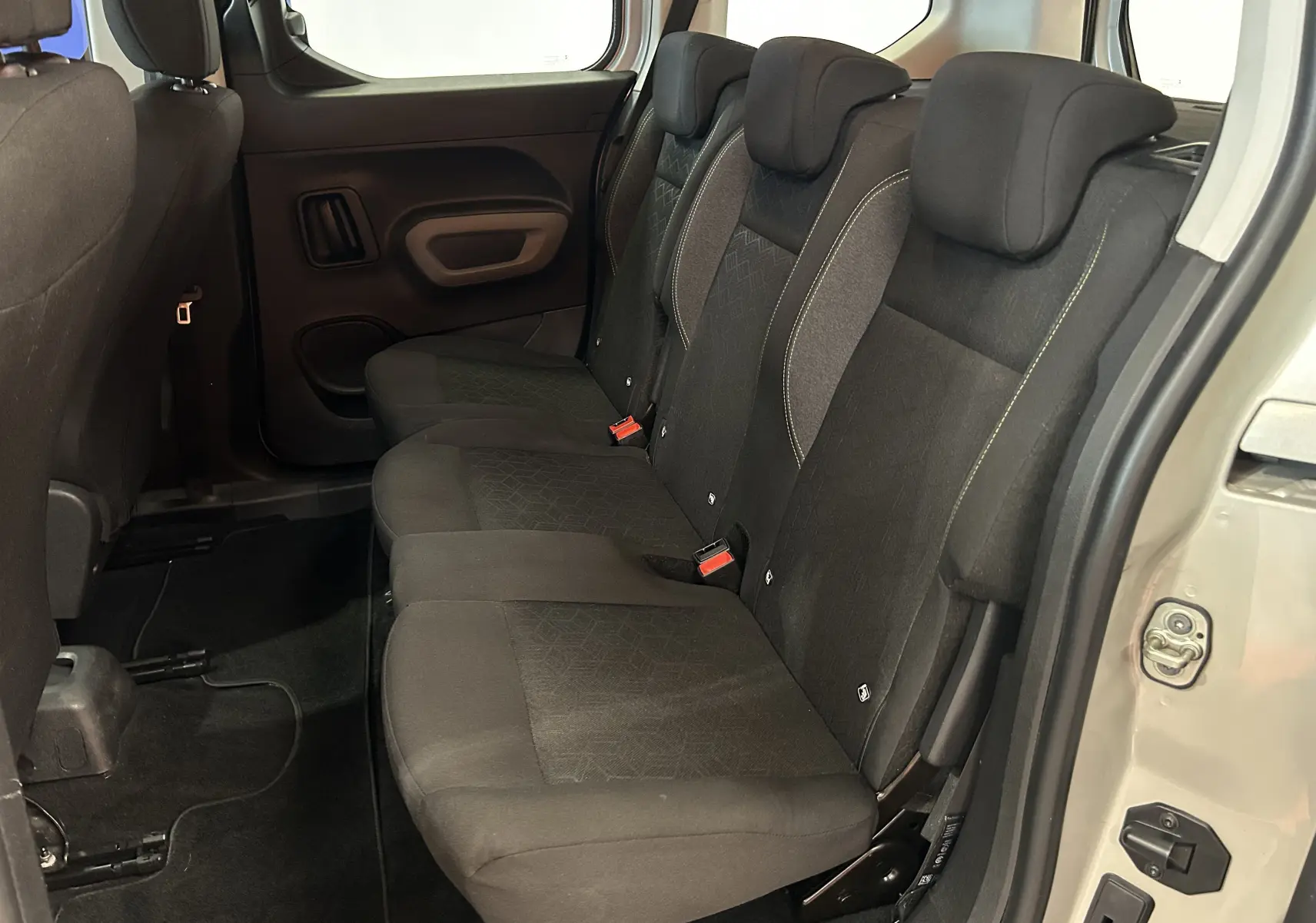 Vue latérale droite de l'intérieur arrière du Peugeot Rifter 2019, sièges tissu noirs avec appuie-têtes et porte gris sable ouvert.