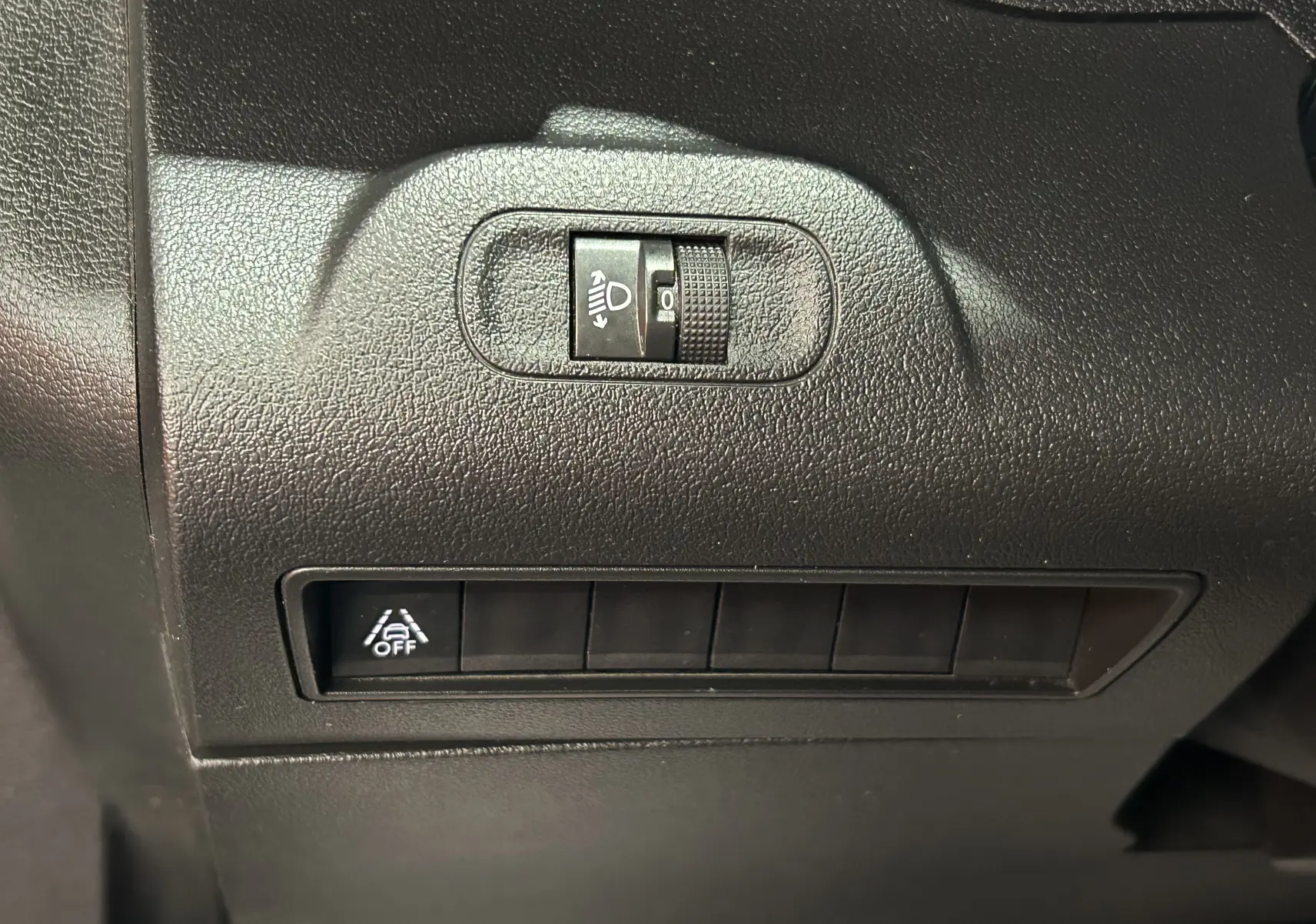 Détail du tableau de bord du Peugeot Rifter gris sable 2019, montrant les commandes d'éclairage et de désactivation de l'assistance.