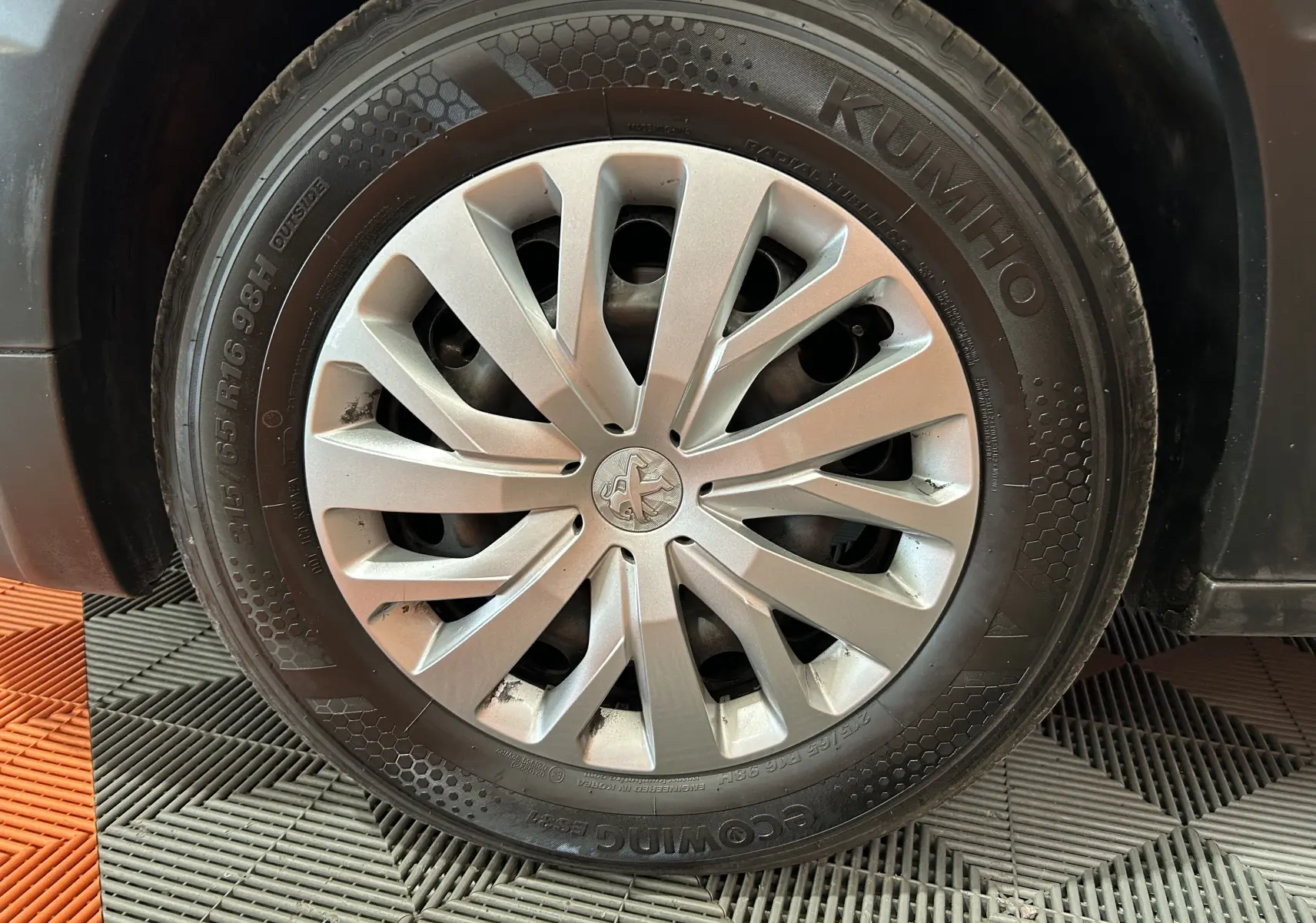 Gros plan sur la roue avant gauche du Peugeot Rifter gris sable, avec jante en alliage et logo Peugeot central.