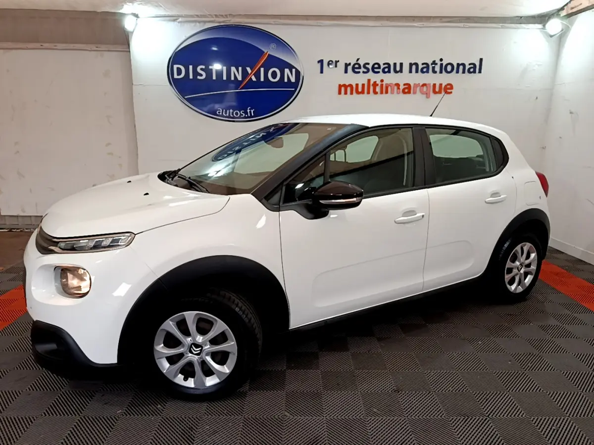 Citroën C3 blanche vue de profil côté gauche, avec feux avant allumés dans un showroom.