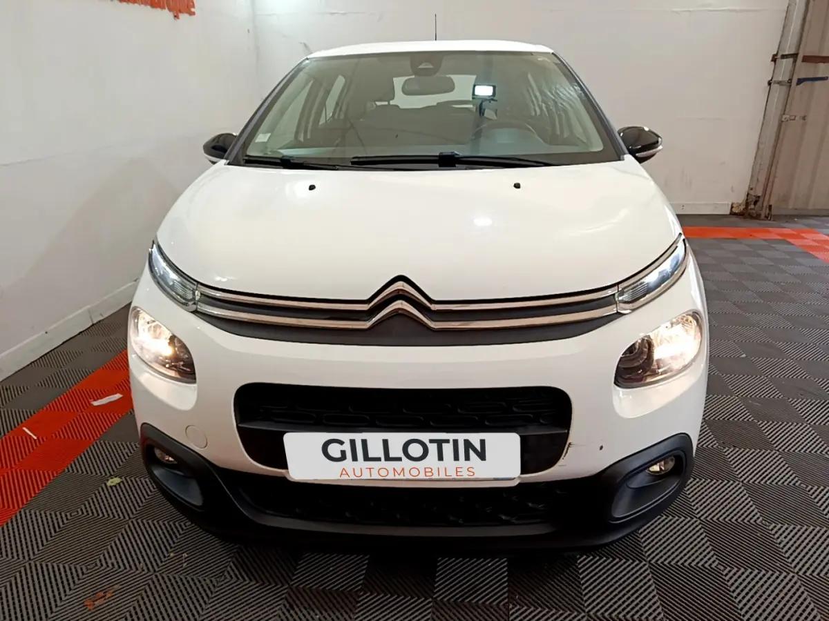 Vue frontale d'une Citroën C3 blanche de 2019 avec phares allumés dans un garage intérieur.