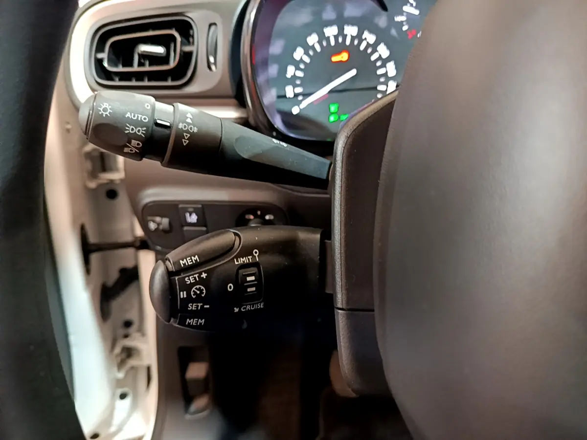 Gros plan sur les commandes du régulateur de vitesse et des phares côté gauche du volant d'une Citroën C3 blanche de 2019.