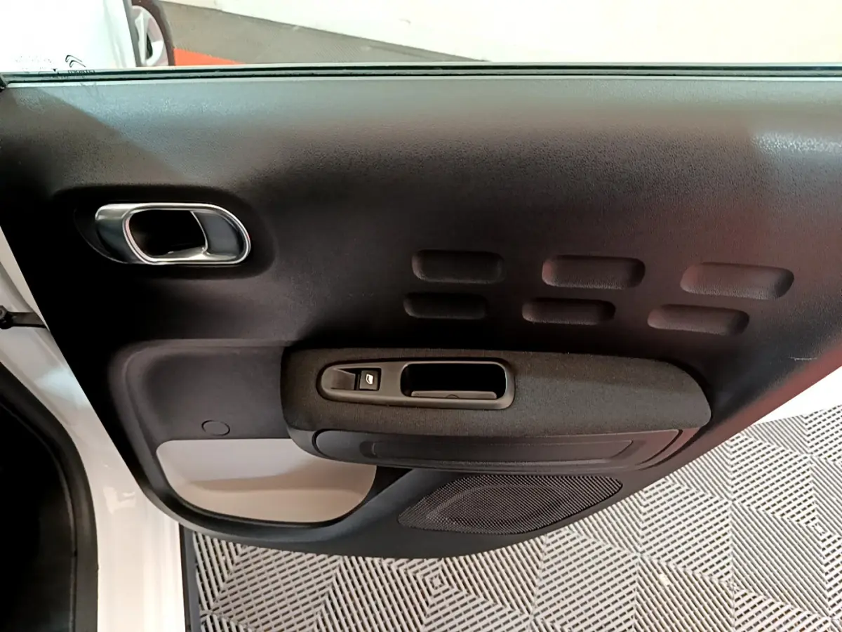 Vue intérieure de la porte côté gauche d'une Citroën C3 blanche, avec poignée et commande de fenêtre noire.