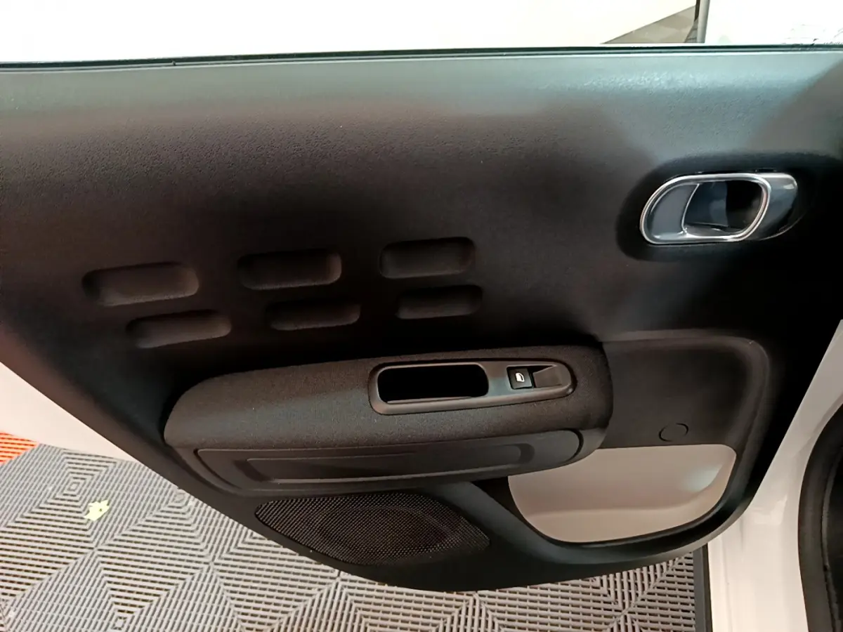 Gros plan sur la porte intérieure côté droit de la Citroën C3 blanche, avec poignée chromée et bouton de verrouillage.