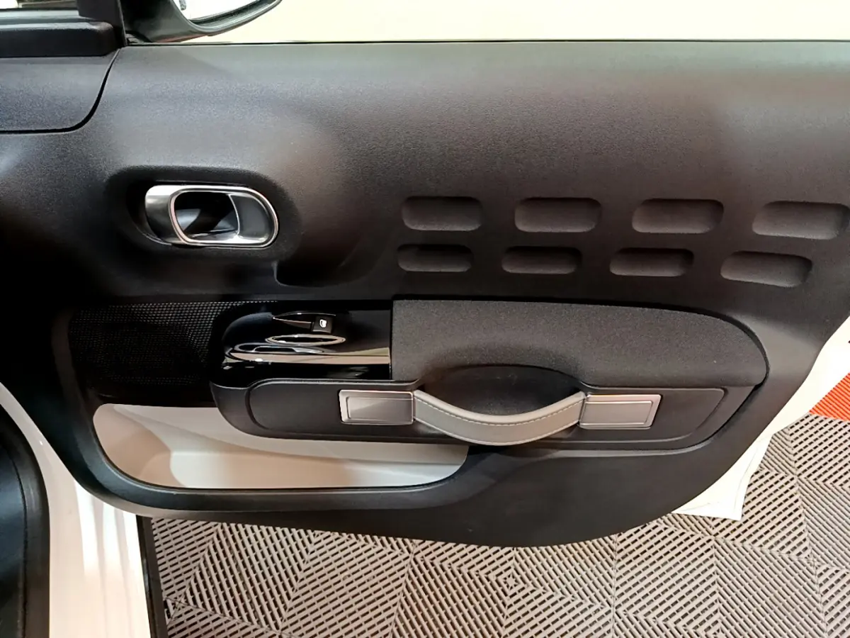 Gros plan sur la porte côté gauche intérieure noire et blanche de la Citroën C3 blanche avec poignée et commandes vitrées.