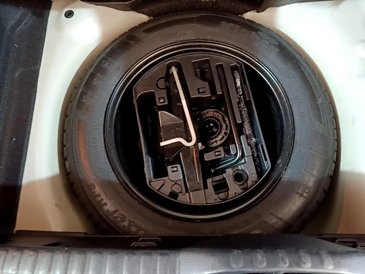 Vue plongeante sur la roue de secours noire et ses outils dans le coffre blanc d'une Citroën C3 2019.