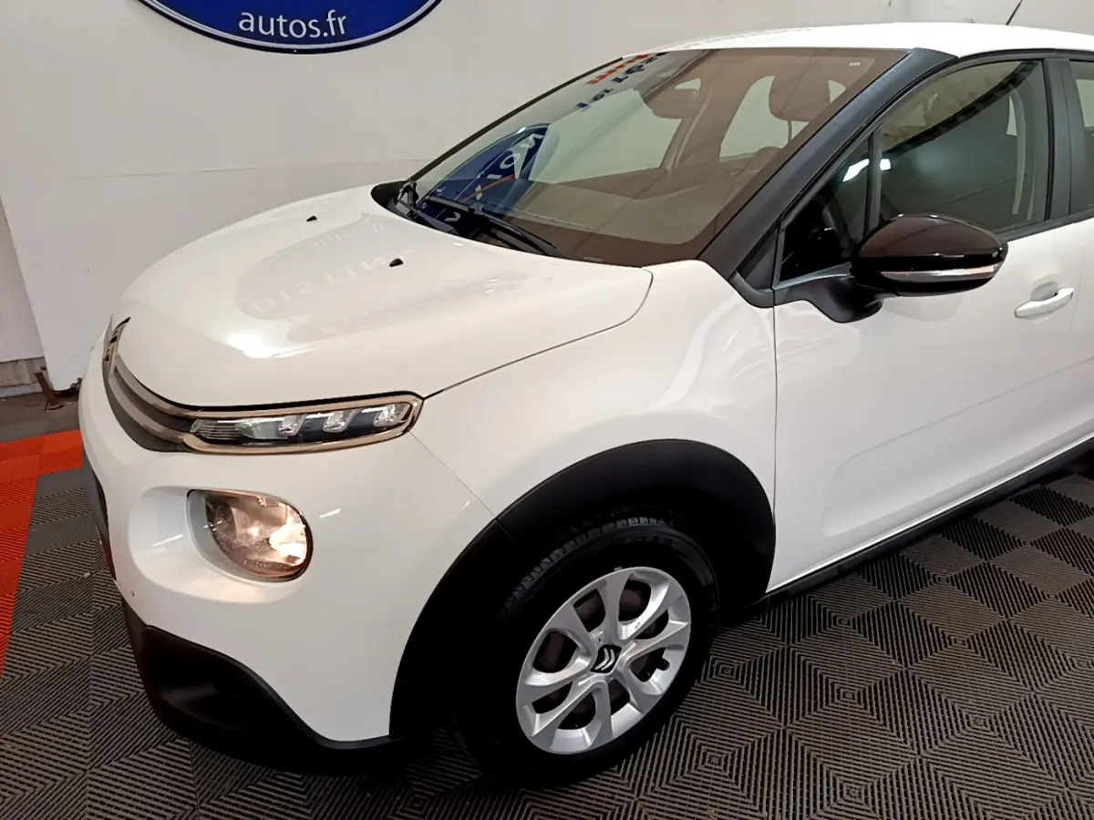 Vue 3/4 avant droit d'une Citroën C3 blanche avec phares allumés et rétroviseurs noirs contrastants.