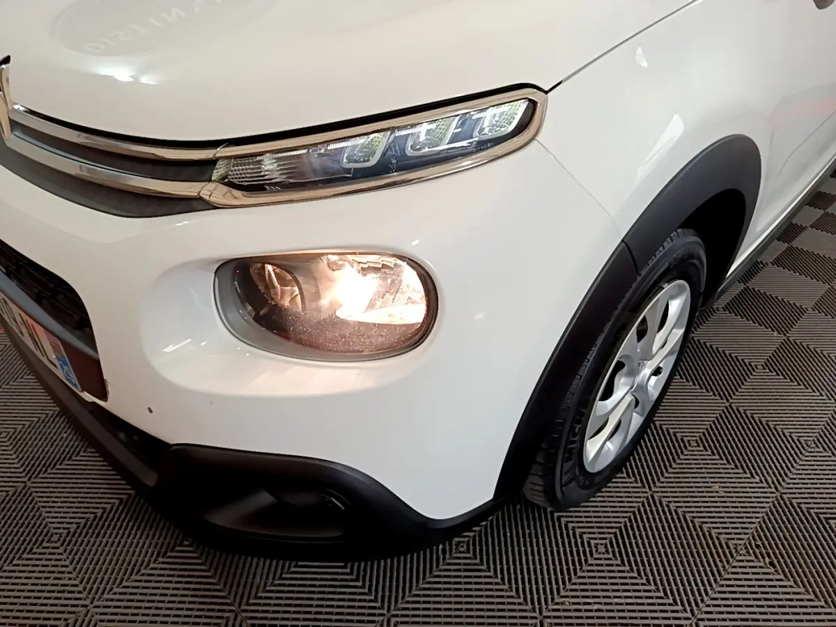 Gros plan sur l'avant droit blanc d'une Citroën C3 2019 avec phares allumés et jante alu visible.