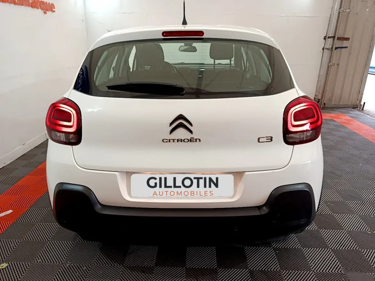 Vue arrière d'une Citroën C3 blanche de 2019 avec feux arrière allumés et logo centré sur le hayon.
