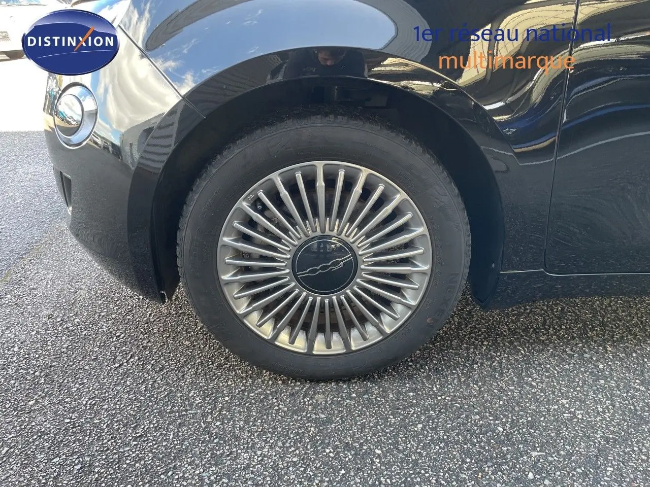 Gros plan sur la roue avant gauche noire d'une FIAT 500 électrique 2023 avec jante argentée à rayons fins.