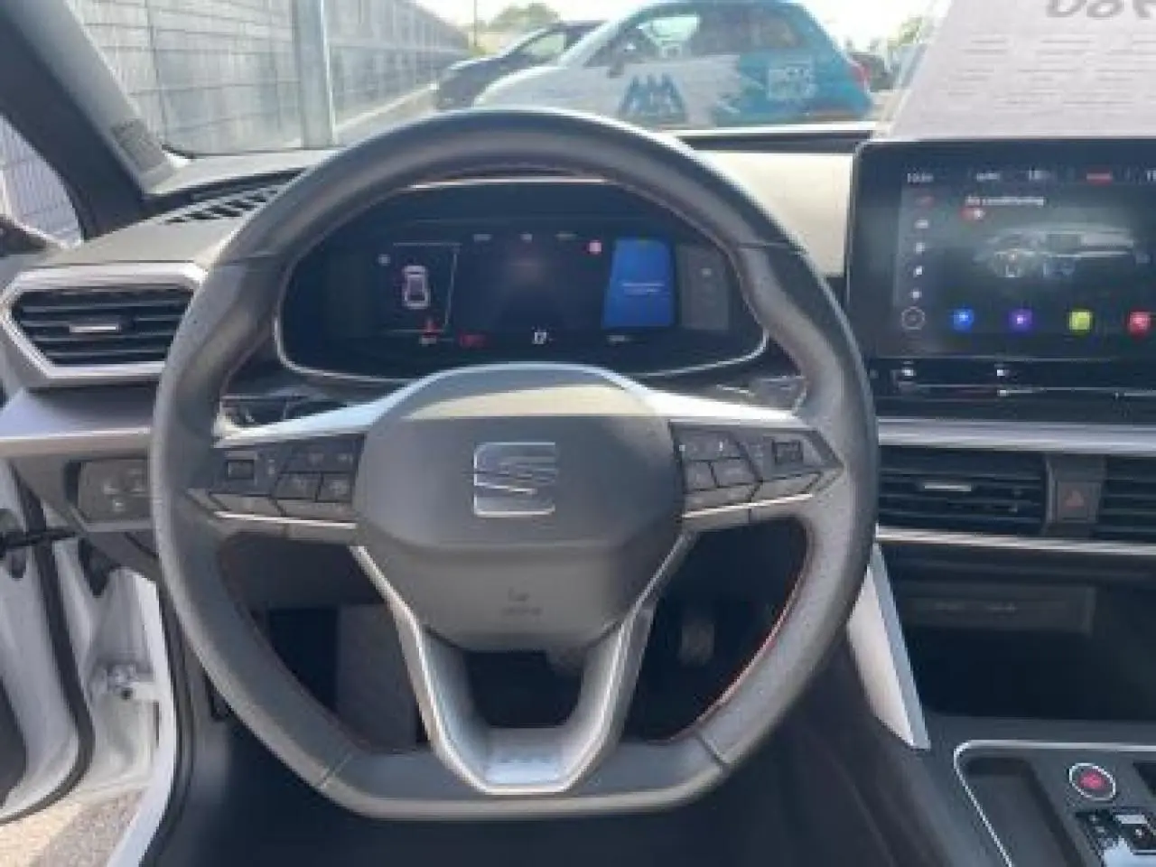 Vue frontale du volant et du tableau de bord digital de la SEAT LEON IV blanche avec écran tactile et commandes au volant.