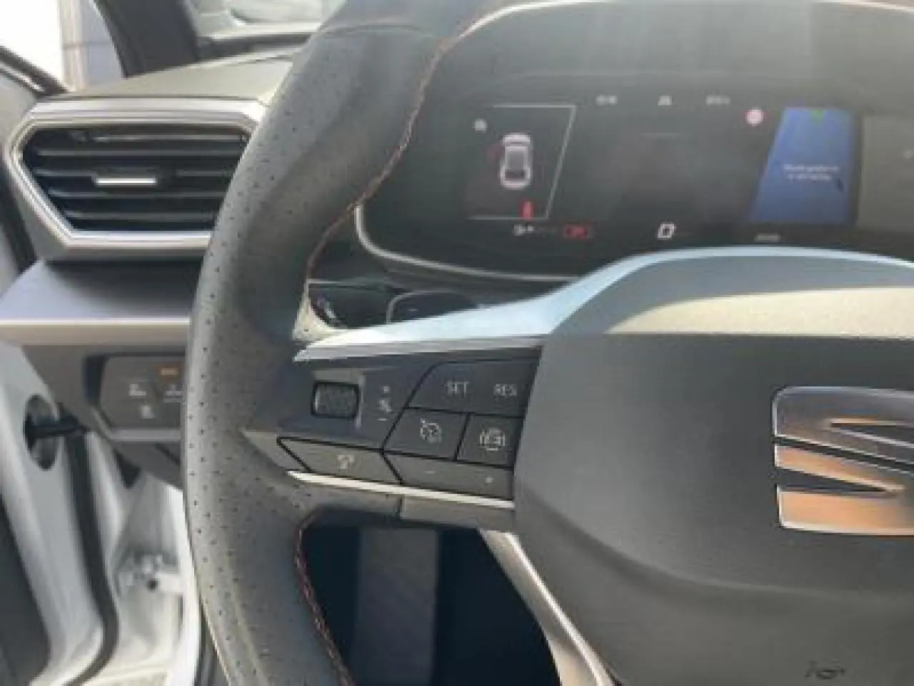 Volant perforé avec surpiqûres rouges et logo SEAT, tableau de bord digital du SEAT Leon blanc Nevada 2024.