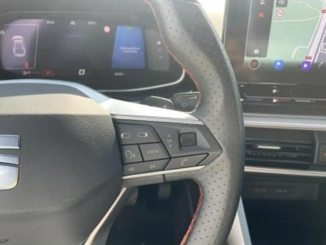 Gros plan sur le volant perforé avec surpiqûres rouges et le tableau de bord digital du SEAT Leon IV blanc Nevada 2024.