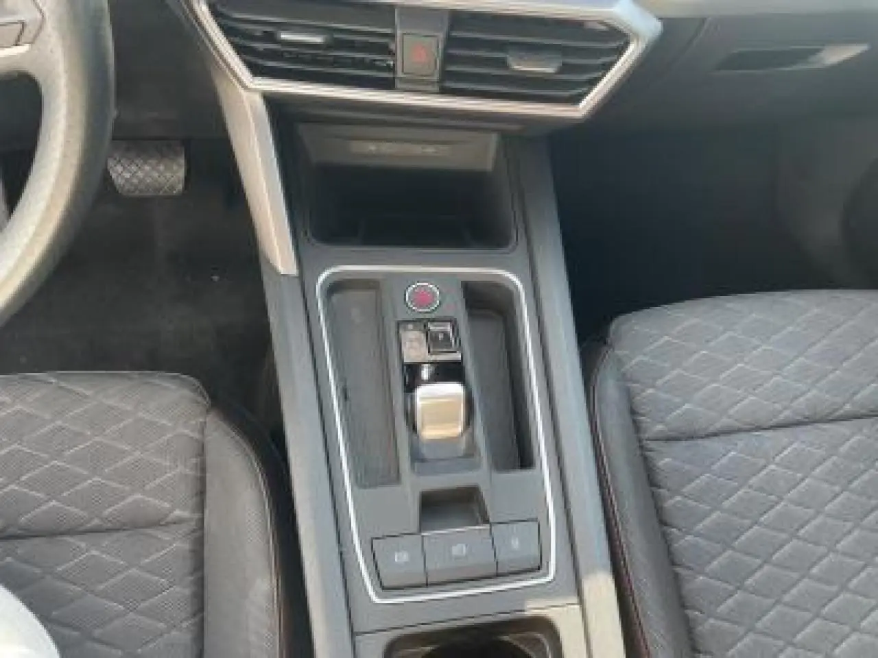 Vue rapprochée de la console centrale de la SEAT LEON IV blanche, avec levier de boîte auto et sièges sport noirs à surpiqûres rouges.