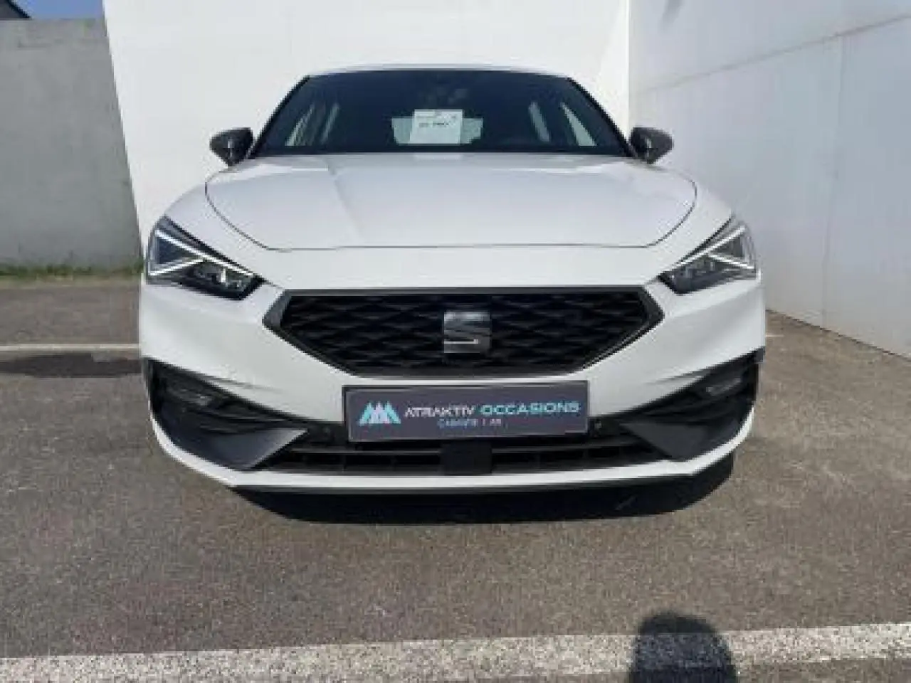 Vue frontale d'une SEAT Leon IV blanche Nevada avec calandre noire et phares LED anguleux.