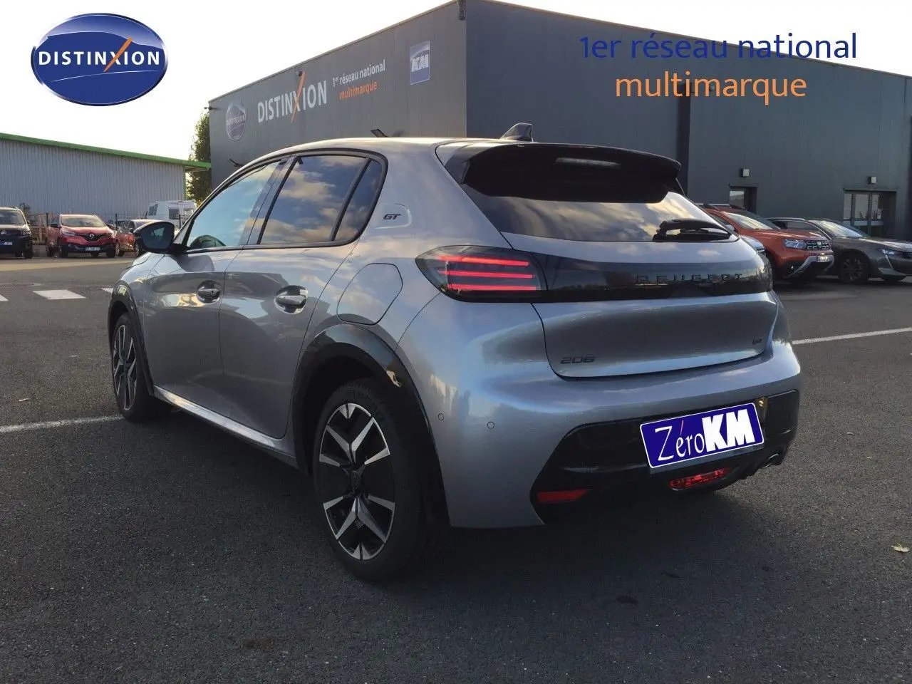 Peugeot 208 gris Artense métal vue 3/4 arrière droit, feux arrière LED et badge GT visibles sur parking.