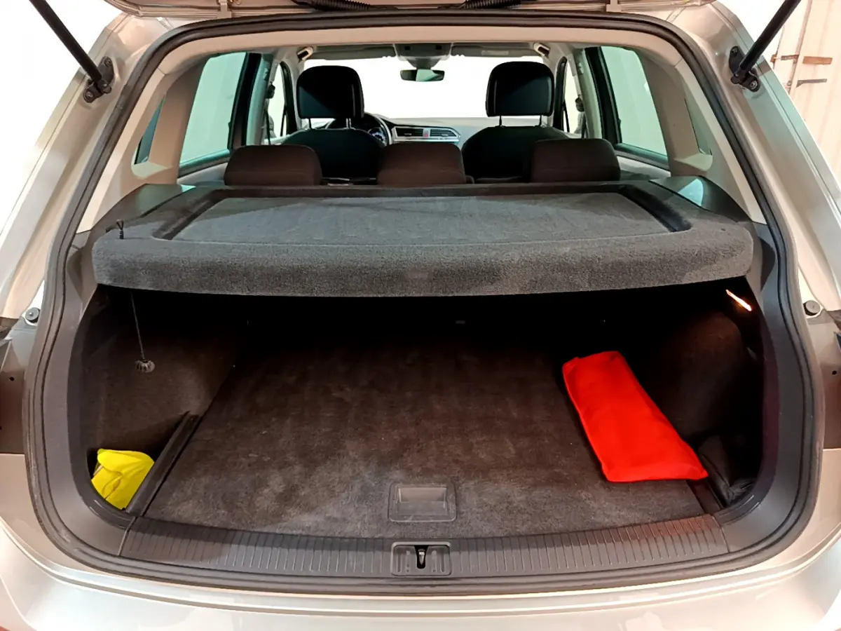 Coffre ouvert vu de l'arrière d'un Volkswagen Tiguan gris clair avec cache-bagages et objets rouges et jaunes.