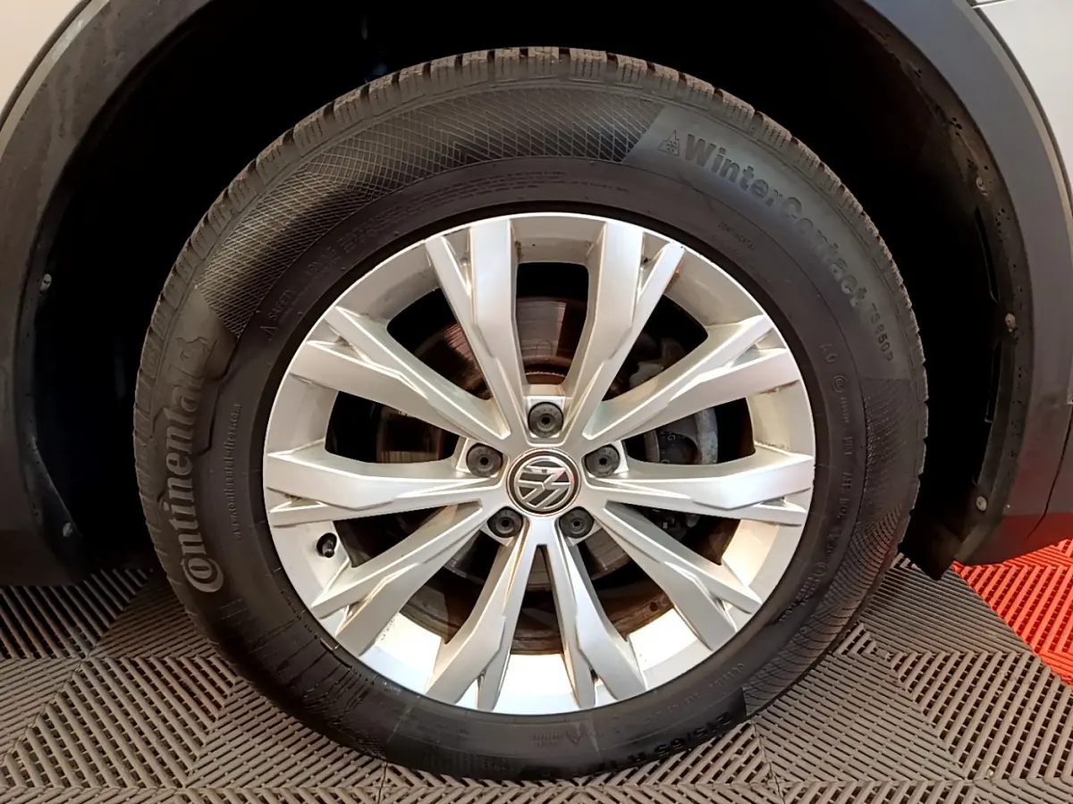 Gros plan sur la roue avant droite d'un Volkswagen Tiguan gris clair avec jante alliage et pneu Continental hiver.