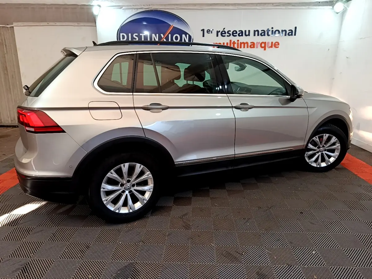 Vue de profil côté gauche d'un Volkswagen Tiguan gris clair 2020 sur sol damier en intérieur showroom.